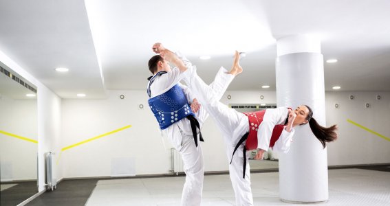 Eine Frau und ein Mann in weißen Anzügen und Schutzwesten trainieren Beintechniken des Taekwondo 