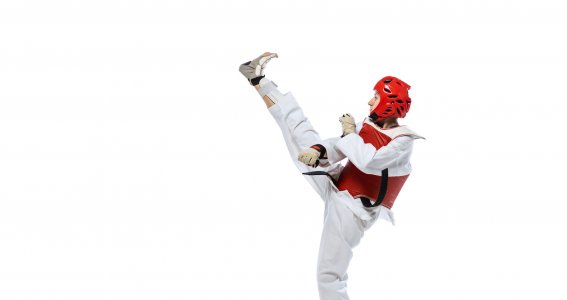 Ein Jugendlicher in Schutzweste und Helm des Taekwondo übt Fußtritte