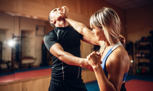 Eine Frau in einer Sporthalle wehrt einen Trainings-Angriff eines Mannes ab