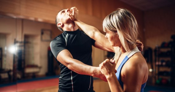 Eine Frau in einer Sporthalle wehrt einen Trainings-Angriff eines Mannes ab