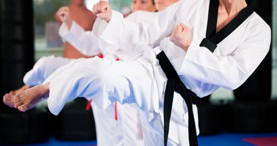 Drei Personen in weißen Taekwondo-Anzügen stehen nebeneinander und setzen zu einem Fußtritt an