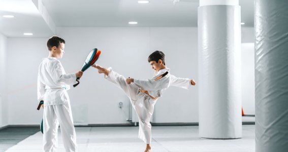 Zwei Jungen trainieren in weißen Taekwondo-Anzügen in einem leeren, weißen Sportraum