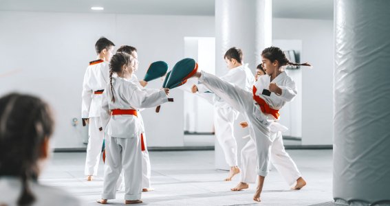 Mehrere Kinder in weißen Anzügen trainieren in Paaren Taekwondo