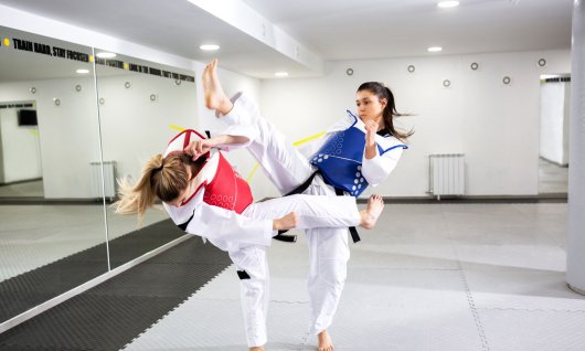 Zwei junge Frauen trainieren mit Schutzausrüstung Taekwondo in einem leeren Sportraum