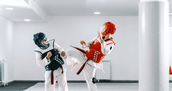 Zwei Jungs mit Helmen und Schutzwesten trainieren Taekwondo in einem gepolstertem Sportraum