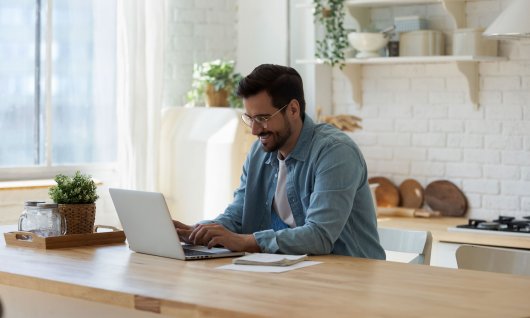 Mann sitzt vor seinem Laptop und lächelt 