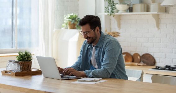 Mann sitzt vor seinem Laptop und lächelt 