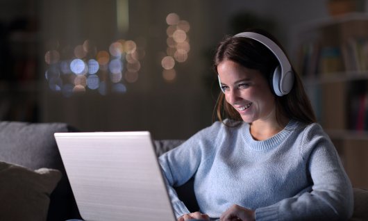 Frau trägt Kopfhörer und schaut auf ihrem Laptop