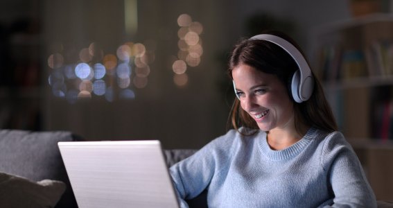 Frau trägt Kopfhörer und schaut auf ihrem Laptop