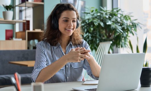 Frau trägt ein Headset und arbeitet am Laptop
