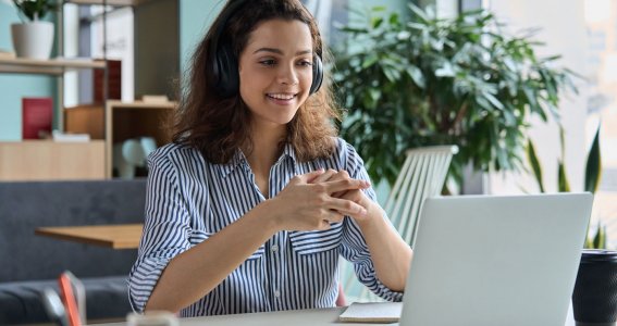 Frau trägt ein Headset und arbeitet am Laptop