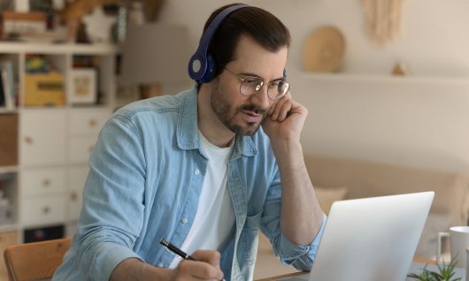 Mann arbeitet am Laoptop und hält einen Stift in der Hand