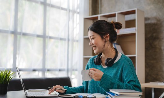 Frau sitzt vorm Laptop und trinkt einen Kaffee