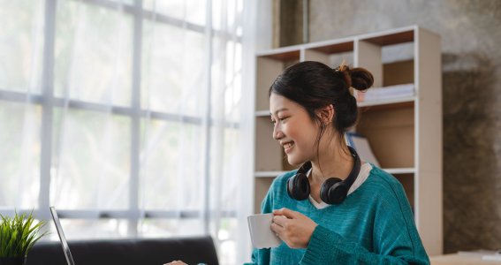 Frau sitzt vorm Laptop und trinkt einen Kaffee