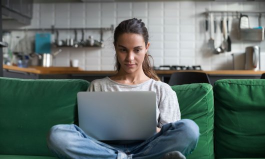Frau sitzt mit Laptop auf einer grünen Couch