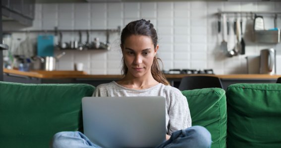 Frau sitzt mit Laptop auf einer grünen Couch