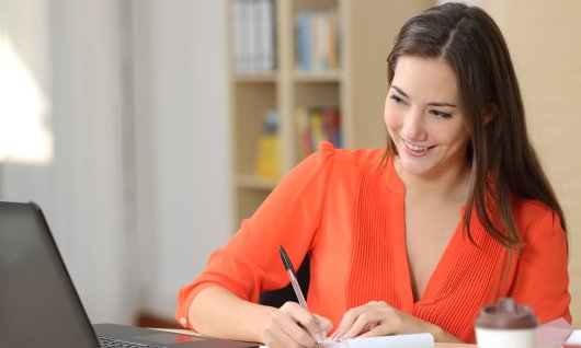 Frau mit orangenem Oberteil schaut den Bildschirm ihres Laptops 