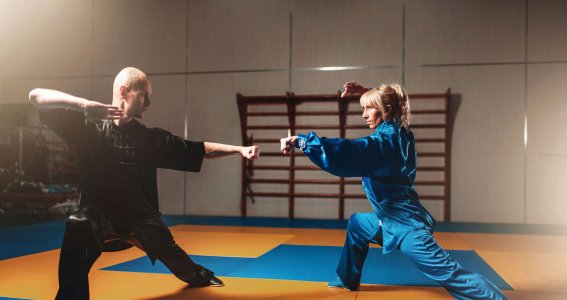 Ein Mann und eine Frau in chinesischer Kleidung trainieren Kampfsport auf einer Matte im Turnsaal