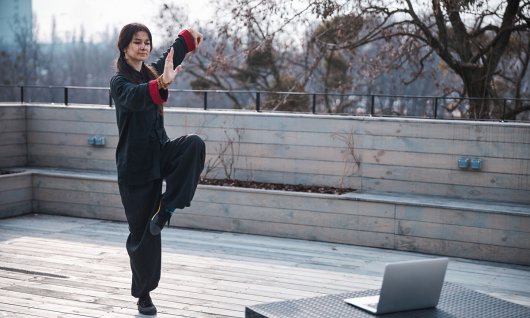 Eine Frau trainiert Kung Fu vor dem Laptop auf einer Dachterrasse 