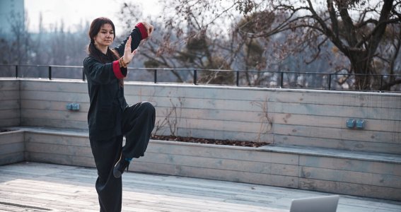 Eine Frau trainiert Kung Fu vor dem Laptop auf einer Dachterrasse 