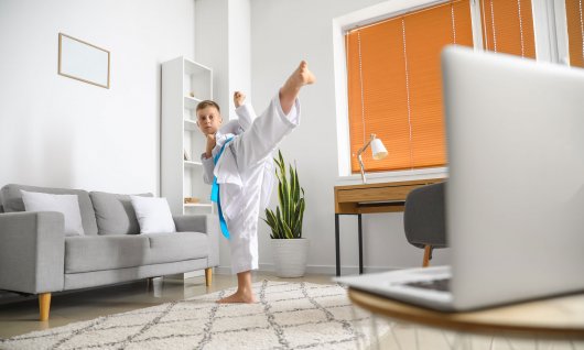 Ein Junge in Kampfpose übt eine Tritttechnik vor dem Computer 