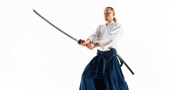 Ein Mann in japanischer Kampfkunstkleidung in Kampfpose mit einem Schwert