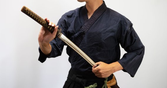 Ein Mann in schwarzer Trainingskleidung zieht ein Katana