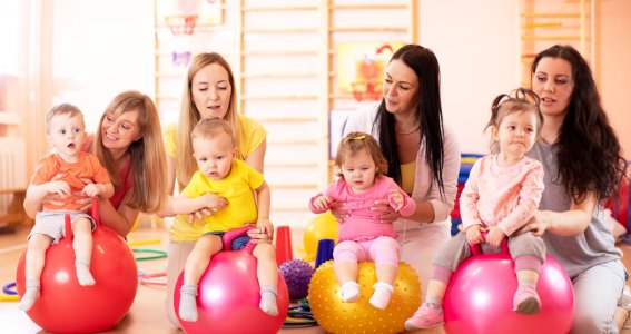 Vier Kinder sitzen auf einem Gymnastikball und die Mütter sitzen hinter ihnen.