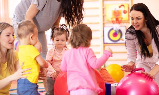 Eltern-Kind-Turnen in Köln Drei kleine Kinder turnen mit ihren Müttern in einer Turnhalle