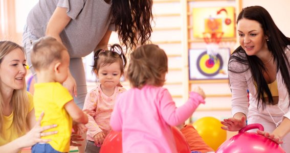 Drei kleine Kinder turnen mit ihren Müttern in einer Turnhalle