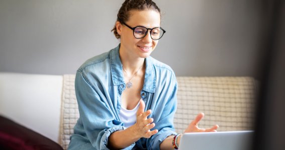 Frau sitzt auf dem Sofa vor einem Laptop. 