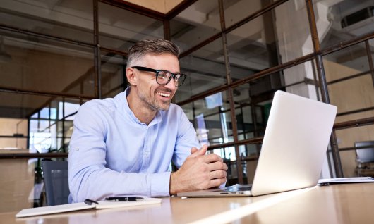 Mann mit Brille sitzt vor Laptop und telefoniert.