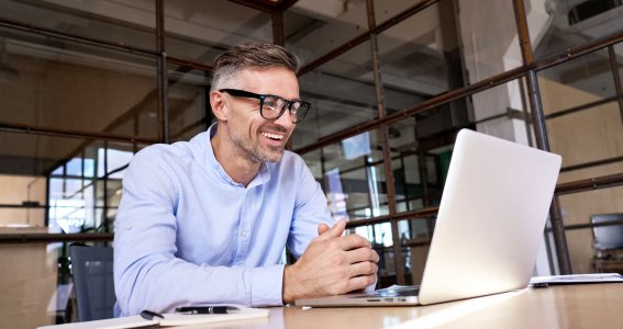 Mann mit Brille sitzt vor Laptop und telefoniert.