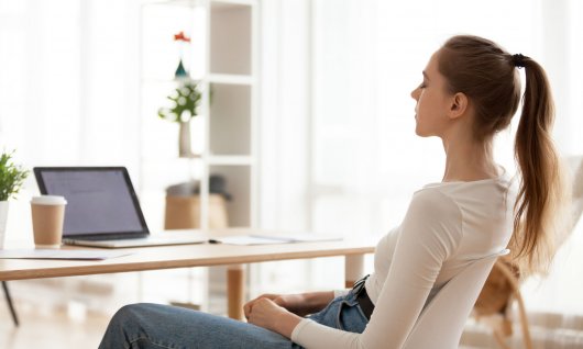 Frau sitzt am Tisch vor Laptop und meditiert. 