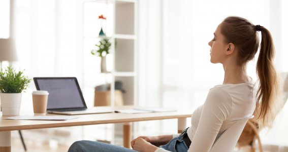 Frau sitzt am Tisch vor Laptop und meditiert. 