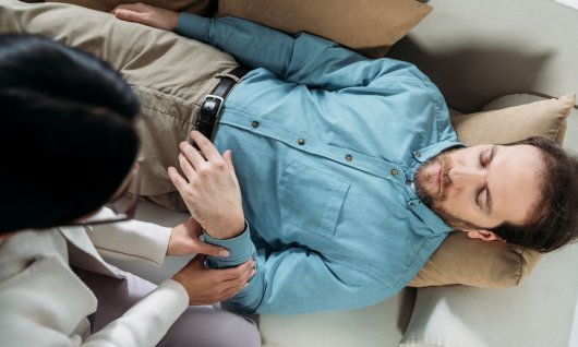 Mann liegt auf dem Sofa und wird hypnotisiert. 