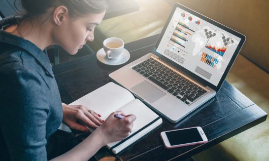 Frau sitzt am Laptop und schreibt etwas auf