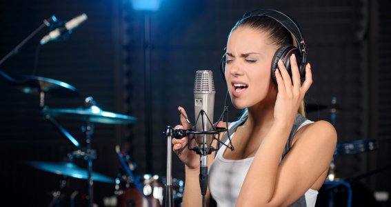 Eine junge Frau mit Kopfhörern singt in ein Mikrofon mit einem Schlagzeug im Hintergrund