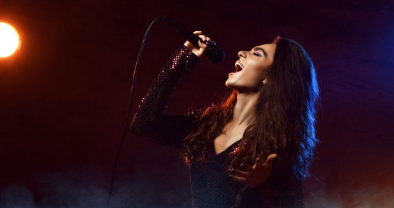 Eine Frau in schönem Kleid steht im Rampenlicht und singt leidenschaftlich in ein Mikrofon