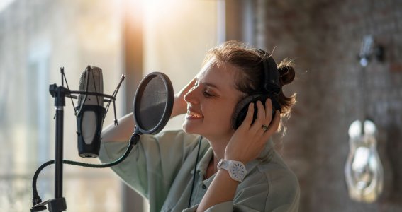 Eine junge Frau singt vor einer Ziegelwand in ein Studiomikrofon