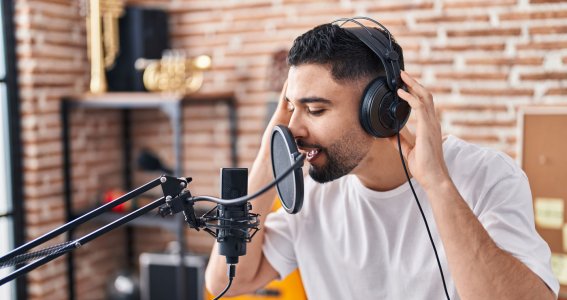 Ein junger Mann vor Ziegelwand singt in ein Studiomikrofon