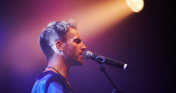 Ein Mann singt in dunkler Atmosphäre im Rampenlicht in ein Mikrofon