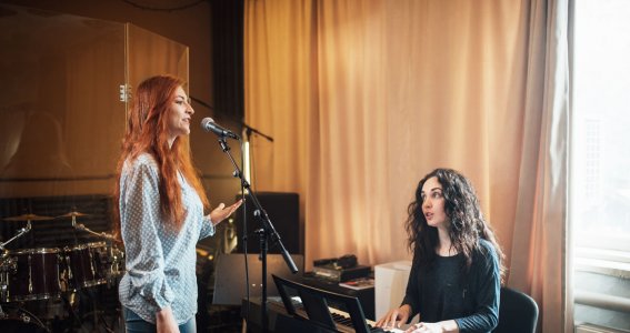 Eine Frau singt in ein Stehmikrofon und eine andere Frau begleitet sie am Keyboard
