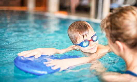 Schwimmlehrerin unterstützt beim Schwimmen lernen mit Schwimmbrett