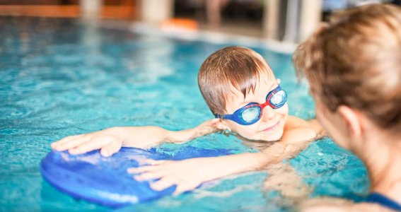 Schwimmlehrerin unterstützt beim Schwimmen lernen mit Schwimmbrett