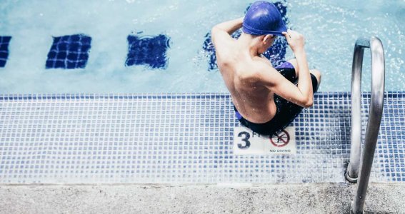 Junge sitzt am Beckenrand und ist bereit zu schwimmen