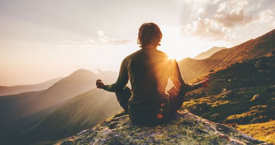 Mann sitzt auf einem Berg bei Sonnenaufgang und macht Yoga