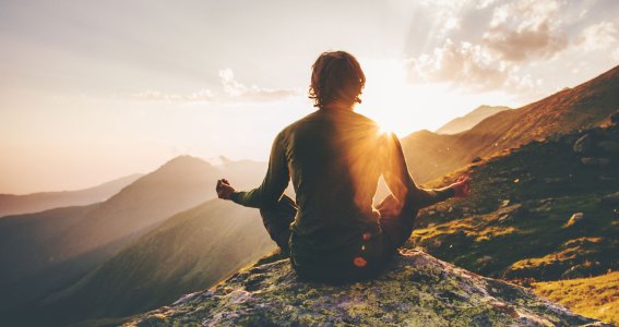 Mann sitzt auf einem Berg bei Sonnenaufgang und macht Yoga