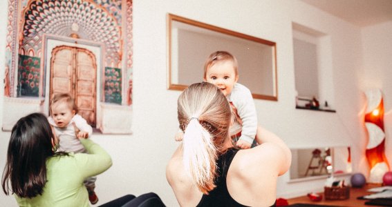 Frauen machen mit ihren glücklichen Babys Yogaübungen