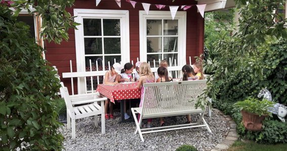 Kinder sitzen vor einem roten Gartenhaus. 